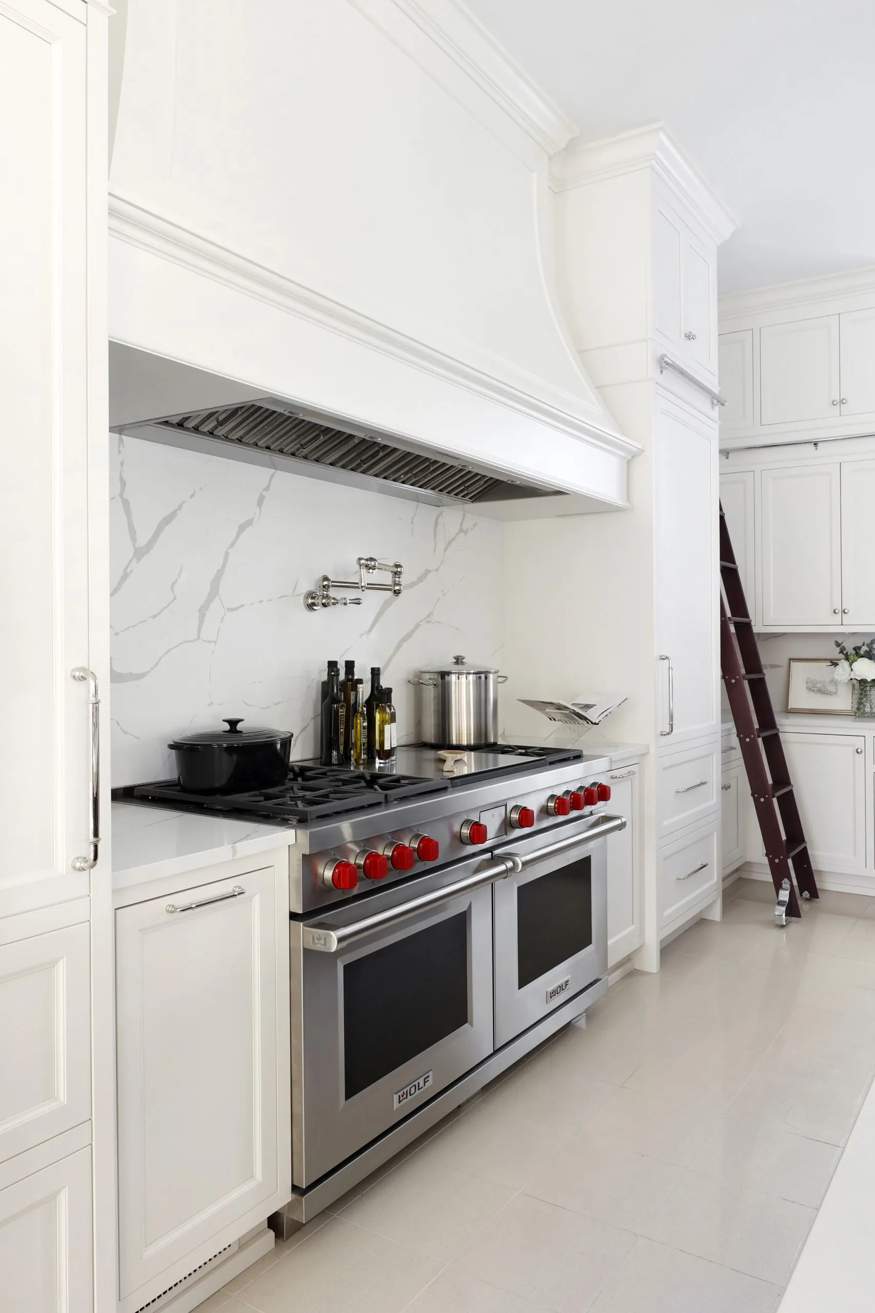 A white kitchen with a professional range and marble backsplash